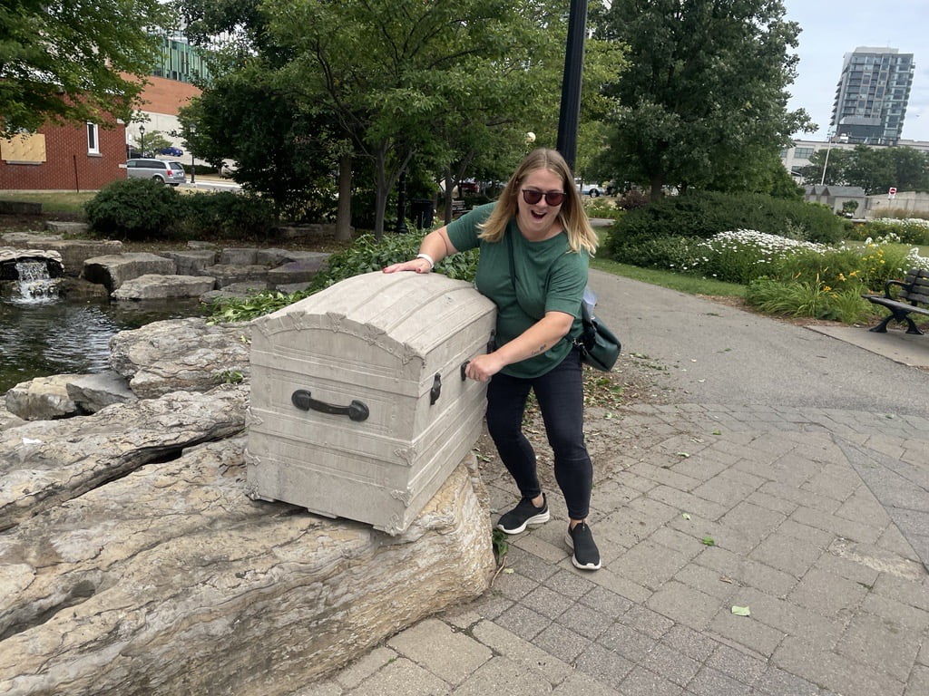 Joanna pretends to pry into a treasure chest sculpture at the entrance of Victoria Park